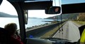 Tourist guide with microphone at front of coach with view of the sea and hills through the windscreen