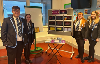 St Columba's school pupils in uniform standing next to a board holding SCQF promotional materials