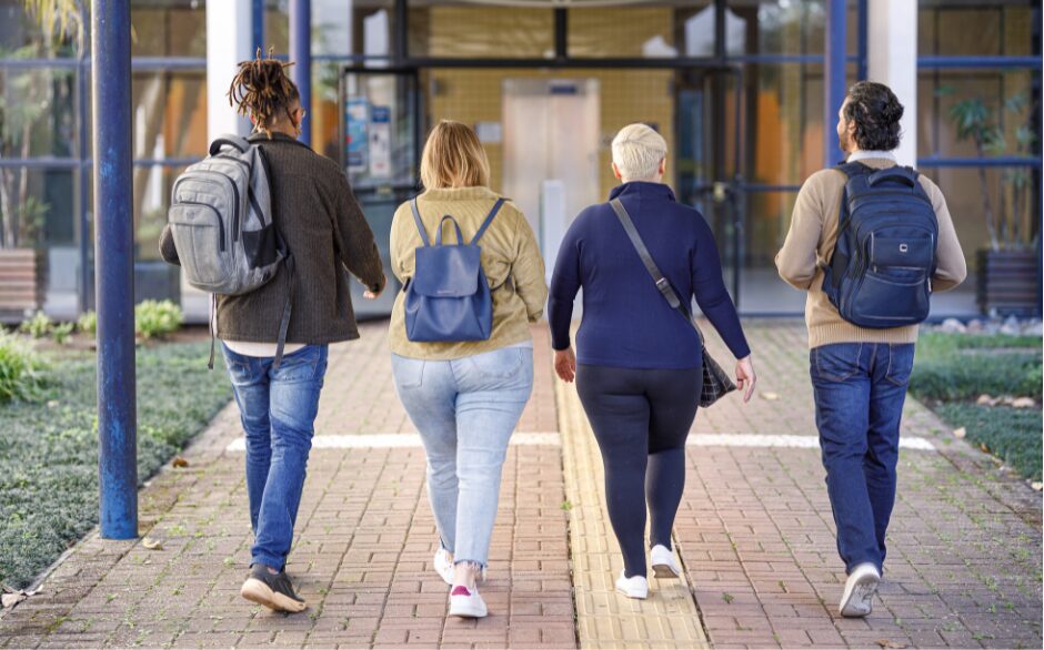 A group of 4 students, who all have bags, walking towards a building. They represent students that the SCQF supports.